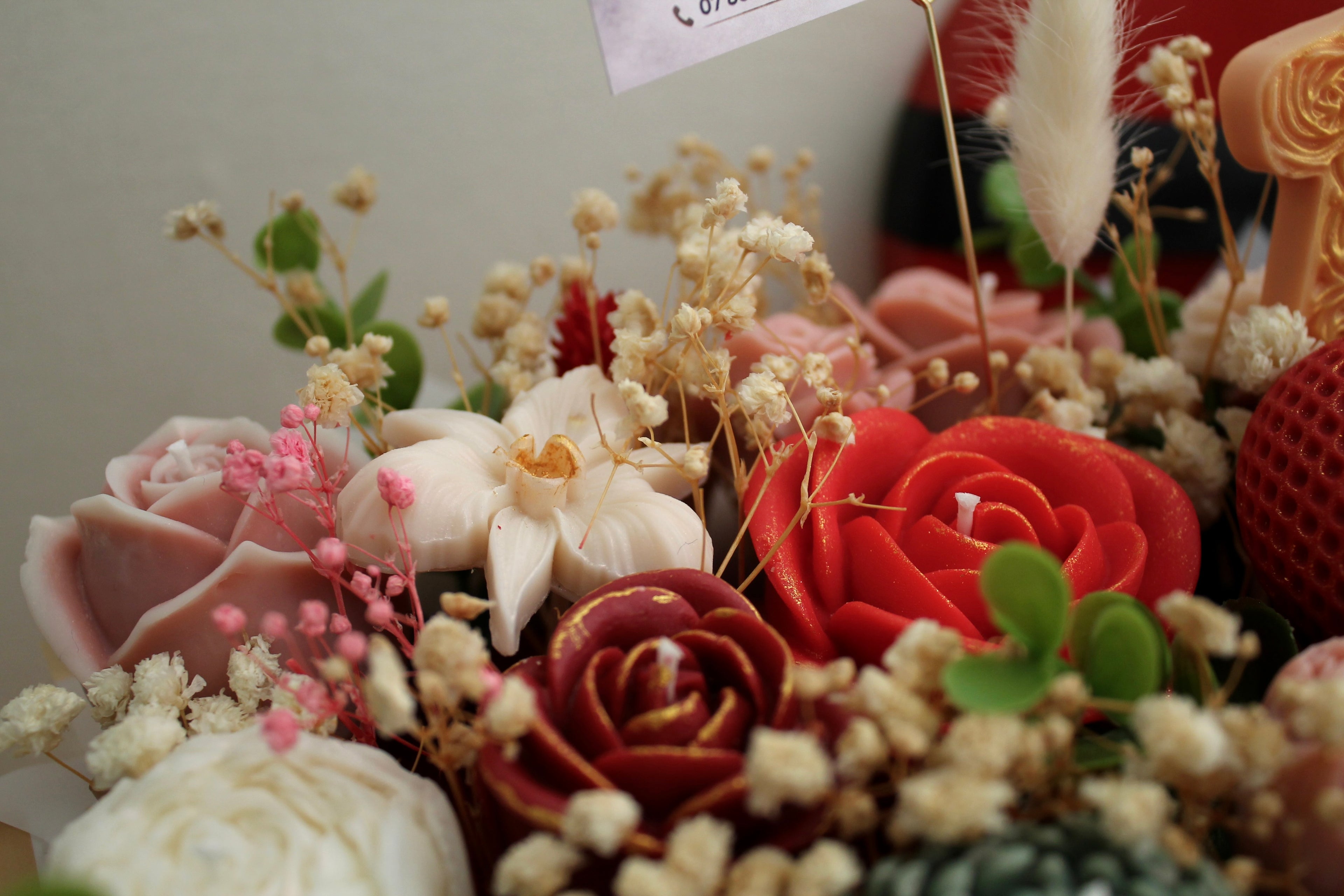 Gros plan sur un bouquet parfumé Fl’Âme Éternelle avec fleurs en cire végétale, roses rouges et poudrées, orchidée blanche et décoration florale artisanale